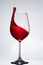 Elegant pure wineglass with wave of brightly red wine standing against light background with reflection in down.