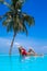 Elegant sexy woman in the red bikini on the sun-tanned slim and shapely body is posing near the swimming pool on Maldives. Perfect