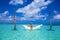 Elegant sexy woman in the white bikini on the sun-tanned slim and shapely body is posing on hammock in ocean on Maldives. Perfect