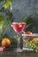 Elegant stemware glass of blood orange cocktail with frozen raspberries in ice cube on dark wooden table surface