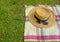 Elegant straw female hat with black ribbon, elegant sunglasses on checkered blanket on grass. top view. summer picnic in the park.