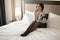 Elegant stylish businesswoman wearing high-heeled shoes lying on bed in hotel