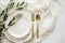 Elegant table setting with white plates, gold cutlery, and olive branch