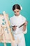 elegant teen artist painting on easel with brush and palette