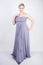 Elegant thick female in a grey long dress. pretty plus size woman in evening dress standing on white studio background. short hair