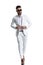 Elegant unshaved guy with sunglasses buttoning white suit and walking