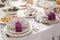 Elegant wedding reception table arrangement, cute purple box with ribbon on white plate near tableware and glasses - luxury