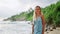 Elegant woman in blue dress strolls on sandy beach, tropical waves in background. Serene lady enjoys ocean breeze