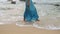 Elegant woman in blue gown walks by sea edge, wading through gentle waves, serene beach scene, tranquil holiday. Female