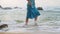 Elegant woman in blue sun dress strolls barefoot by sea. Serene female enjoys peaceful beach walk at sunset. Relaxing