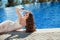 Elegant woman in fashion dress lying by blue swimming pool.