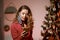 Elegant woman in a red cocktail dress, wearing protective face mask by the christmas tree, alone, lonely, talking and writing on