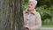 Elegant woman retirement age resting in park alone, standing near large tree, stroking it, touches bark tenderly