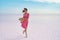 Elegant woman walking by windy serenity landscape of salt flats on pink lake, making step