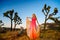 Elegant woman, wearing a fancy dress and standing like a fairy among the Joshua Trees at sunset