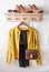 Elegant women`s clothing - black trousers, a yellow jacket, a leather bag, suede chelsea shoes on a hanger in a bright room. Wome