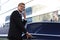 Elegant young businessman entering his car while standing outdoors and talking on smart phone