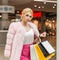 Elegant young fashion model woman in luxurious pink fur coat in leather glamorous fashionable skirt posing in modern store.