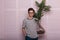 Elegant young man in trendy clothes with glasses stands with an exotic palm tree in a pot near pink wall. Handsome hipster guy in