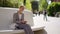 elegant young mixed race woman sitting on stone bench in city square, waiting for someone and using her phone. girl