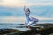 Elegant young woman in beautiful long dress waving in the wind with a deep neckline stay on ocean beach on the rock on sunset