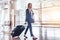 Elegant young woman walking and pulling her suitcase in the airport terminal