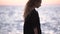 Elegant young woman wanders along beach near blurry sea