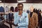 Elegantly dressed African man posing with hand on chin while standing in a classic menswear store.