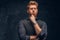 Elegantly dressed redhead man posing with thoughtful look in studio against a dark textured wall