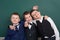 Elementary school boy fooling around near blank chalkboard background, dressed in classic black suit, group pupil, education conce