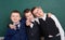 Elementary school boy friends, fooling around near blank chalkboard background, dressed in classic black suit, group pupil, educat