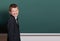 Elementary school boy make faces near blank chalkboard background, dressed in classic black suit, one pupil, education concept