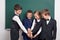 Elementary school boy near blank chalkboard background, dressed in classic black suit, group pupil, education concept