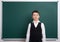 Elementary school boy near blank chalkboard background, dressed in classic black suit, one pupil, education concept