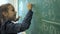 Elementary school. Little schoolgirl writing numbers on green chalk board in classroom