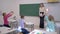 Elementary school, teacher female near blackboard holds an information lesson for schoolchildren sitting at desks in