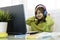 Elementary schooler girl in headphones sitting at desk on laptop - Smiling cute girl studying online from home and learning using