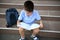 Elementary student doing homework sitting next to his school bag on the stairs of school establishment. Back to school