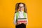 Elementary Student Girl Holding Stack Of Books Over Yellow Background