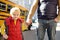 Elementary student hold hands his father near yellow school bus on background