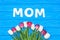 elevated view of bouquet of pink and white tulips and word mom on blue table, mothers day concept