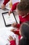 Elevated view of two kindergarten school kids sitting at a desk in a classroom drawing with a tablet computer and stylus, close up