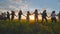 Eleven cheerful girls run to the meeting across the field in the summer, holding hands.