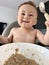 An eleven-month-old baby eats porridge on his own with a spoon while sitting in a high chair