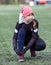 Eleven years old girl football player makes tying shoelaces on cleats, artificial green field