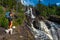 Elgafossen - Algafallet,  Backpacker girl with her dog looks at Waterfall Located between Sweden and Norway