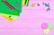 Ellow and green pencils, felt-tip pens, notepaper, paper clips, stationery nails, felt and smiles on pink wooden background