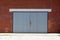 Elongated garage doors made from narrow wooden boards with faded color mounted on red bricks wall