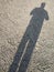 an elongated shadow of a man on a surface with chips & pebbles