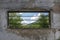 An elongated window with bars in an old building overlooking a beautiful forest and cloudy sky. concept